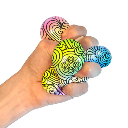 A hand squeezing a NeeDoh Press-Doh. The colorful doh is visible through the white and black designs of the exterior.